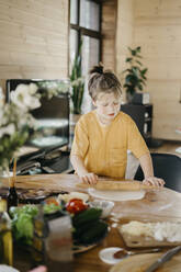 Boy with flour on face flattening dough at home - SEAF00282