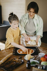 Junge bereitet mit seiner Mutter zu Hause eine Pizza zu - SEAF00284