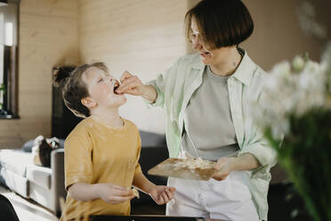 Lächelnde Mutter, die ihrem Sohn geriebenen Käse füttert, der mit Mehl im Gesicht bedeckt ist - SEAF00285