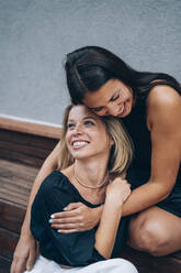 Glückliche Frauen umarmen sich auf einer Bank sitzend - OMIF00271