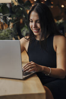 Young woman using laptop sitting in cafe - OMIF00282