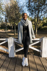 Happy teenage girl leaning on railing at boardwalk - JRVF02316