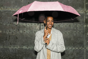 Teenager-Mädchen mit Regenschirm vor einer schwarzen Wand stehend - JRVF02336