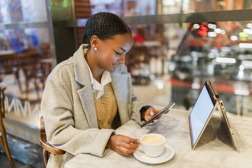 Teenager-Mädchen mit Kaffeetasse und Smartphone am Laptop im Café - JRVF02351