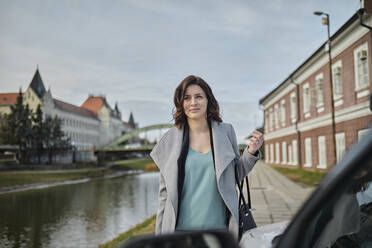 Frau in Jacke trägt Handtasche durch Auto auf Gehweg - ZEDF04304