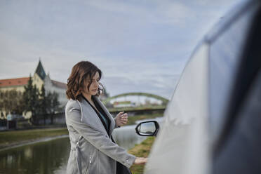 Woman in jacket opening door of electric car - ZEDF04305