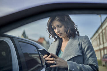 Woman using mobile phone at open car door - ZEDF04307