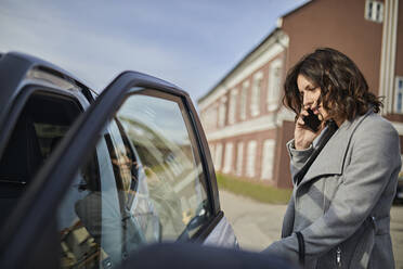 Frau, die mit dem Handy spricht und die Autotür öffnet - ZEDF04308