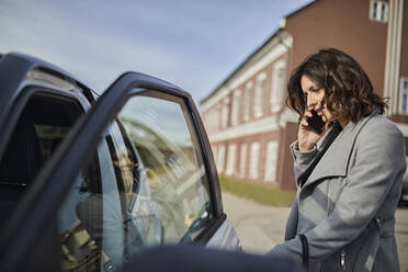 Woman talking on mobile phone and opening car door - ZEDF04308