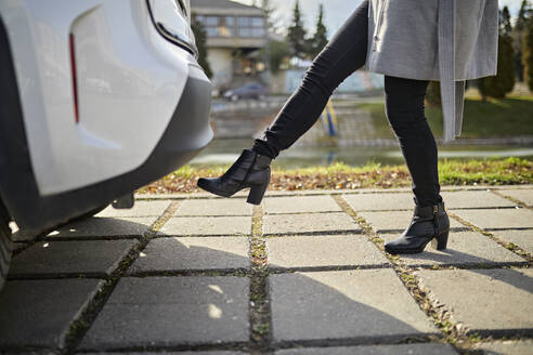 Frau öffnet Kofferraum eines Autos mit Fußsensor auf Gehweg - ZEDF04314