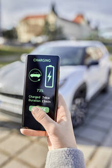 Woman checking electric car charging status through mobile phone - ZEDF04321