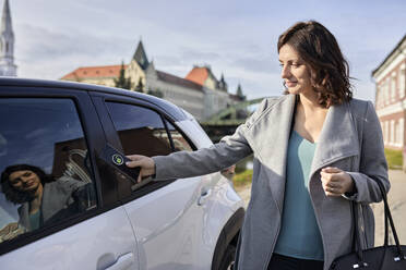 Woman unlocking electric car through smart phone on sunny day - ZEDF04323