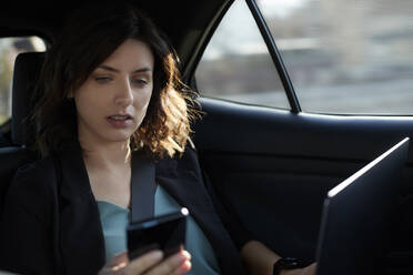 Businesswoman with laptop using mobile phone in driverless car - ZEDF04339