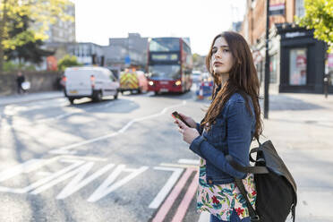 Woman with smart phone waiting at roadside in city - WPEF05641