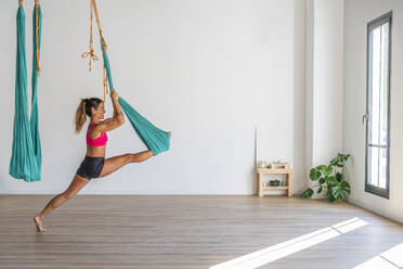 Flexible Frau, die sich in einem Yogastudio auf Seide dehnt - DLTSF02474