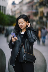 Junge Frau benutzt Mobiltelefon auf dem Gehweg - OCMF02298