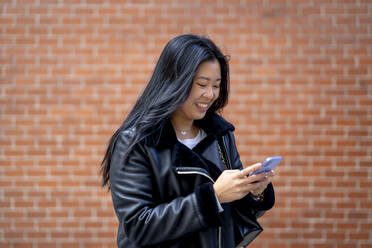 Woman using smart phone in front of wall - OCMF02301