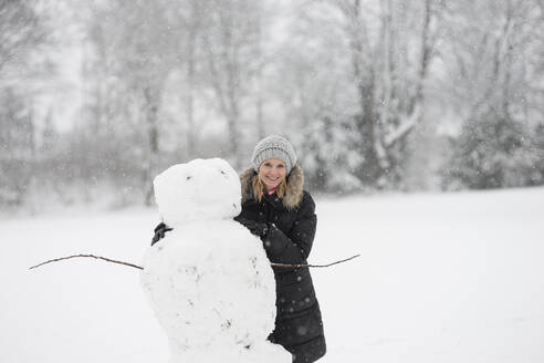 Lächelnde Frau mit Schneemann im Winterpark - CHPF00819