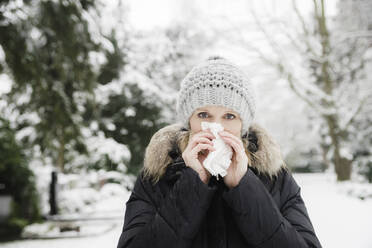 Woman blowing nose with facial tissue in winter park - CHPF00820
