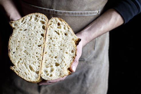 Bäcker hält halbierten Laib Brot in der Bäckerei - IFRF01296