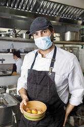 Koch mit Gesichtsschutzmaske hält Dessertschale in Restaurantküche - IFRF01314