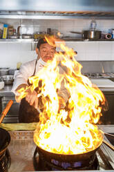 Chefkoch kocht in flammendem Wok in Restaurantküche - IFRF01319