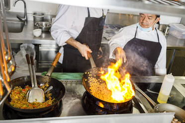 Chefkoch unterrichtet Kollege, der Essen im Wok in der Küche anzündet - IFRF01320