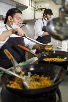 Köche mit Gesichtsmaske bei der Zubereitung von Speisen in einer Restaurantküche - IFRF01321