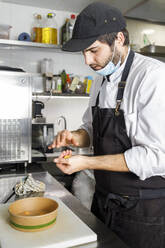 Koch mit Gesichtsmaske bei der Zubereitung von Essen zum Mitnehmen - IFRF01323