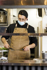 Koch mit Schutzmaske beim Schärfen von Messern in der Küche - IFRF01330