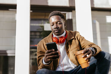 Young man holding reusable cup using smart phone - TCEF02121