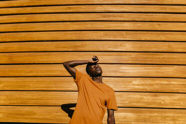 Junger Mann mit geschlossenen Augen vor einer orangefarbenen Wand bei Sonnenuntergang - TCEF02125