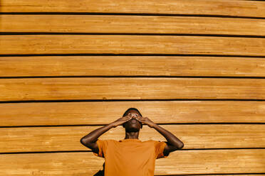 Mann mit Händen, die die Augen bedecken, vor einer orangefarbenen Wand bei Sonnenuntergang - TCEF02131