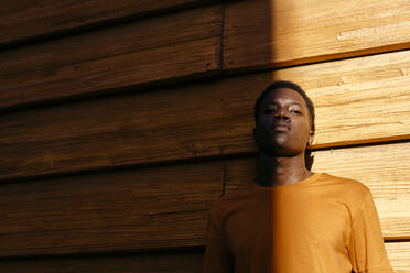 Junger Mann vor einer orangefarbenen Wand bei Sonnenuntergang - TCEF02135