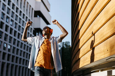 Carefree man with arms raised enjoying music dancing in city at sunset - TCEF02141