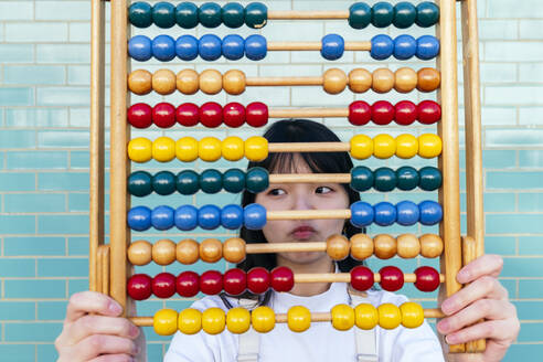 Woman with multi colored abacus puckering in front of brick wall - ASGF01971