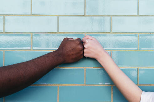 Multirassische Freunde, die sich an einer türkisfarbenen Backsteinmauer die Hände reichen - ASGF02027