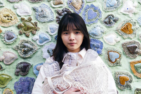 Young woman holding mesh bag with plastic bottles in front of carved wall - ASGF02031