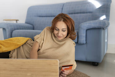 Frau bei Online-Zahlung auf Laptop mit Kreditkarte zu Hause - JCCMF04817