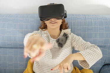 Frau gestikuliert mit Virtual-Reality-Headset zu Hause - JCCMF04840
