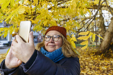 Senior woman taking selfie on smart phone in autumn park - IHF00721