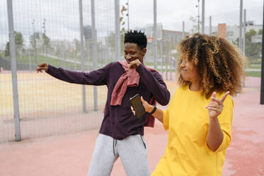 Junge Frau tanzt mit Freundin auf einem Sportplatz - VYF00794