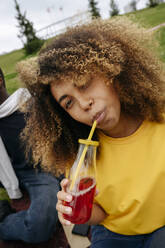 Young woman drinking lemonade by friend in park - VYF00817
