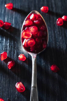 Von oben rote frische saftige Granatapfelfrüchte Samen auf Löffel und dunkle Holzoberfläche auf blauem Hintergrund - ADSF32799