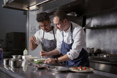 Black cook adding salt to salad making by professional chef in kitchen of restaurant of haute cuisine - ADSF32919