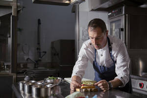 Ein erfahrener männlicher Koch in Uniform bereitet ein Eclair als Vorspeise auf einem Holzbrett in einem Restaurant mit gehobener Küche zu - ADSF32922
