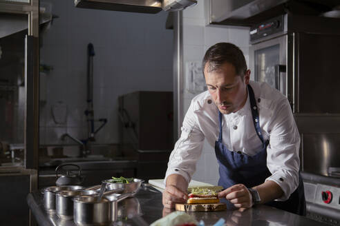 Precise experienced male chef in uniform preparing eclair as appetizer on wooden board in restaurant offering haute cuisine - ADSF32922