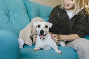 Girl sitting with disabled dog on sofa at home - SEAF00304