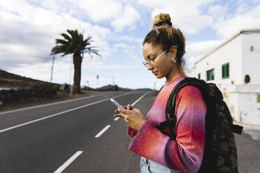 Young woman using mobile phone on roadside - MRAF00811