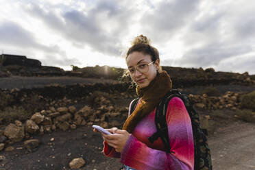 Backpacker holding mobile phone at sunset - MRAF00820